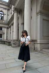a lady in a white cardigan with black trim and a black skirt